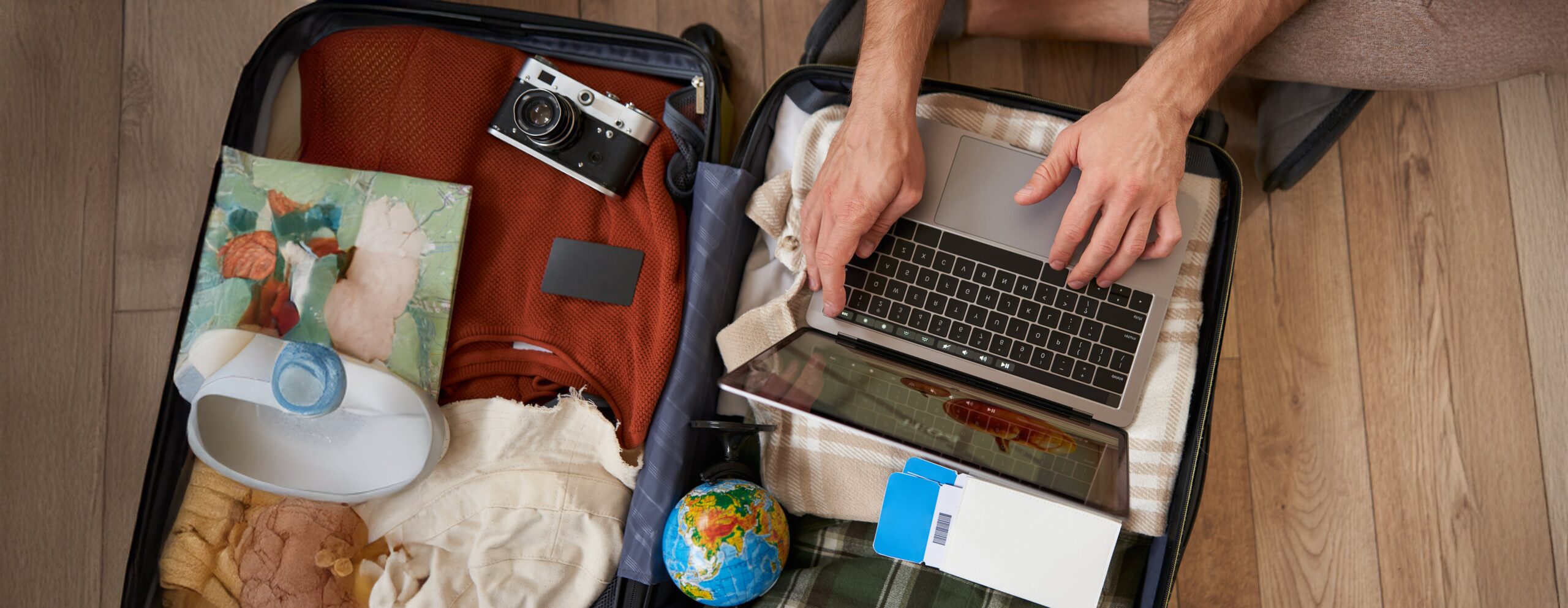 close up portrait of male hands using laptop on top of opened suitcase, man packing for holiday, tourist with globe, booking vacation on travel agency website, picking a tour